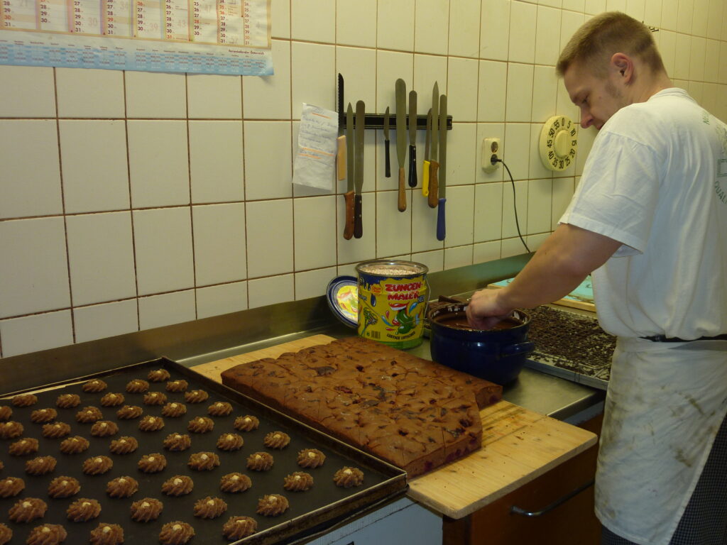 Bäcker taucht Gebäckstücke in Schokolade in der Backstube der Bäckerei Sachse