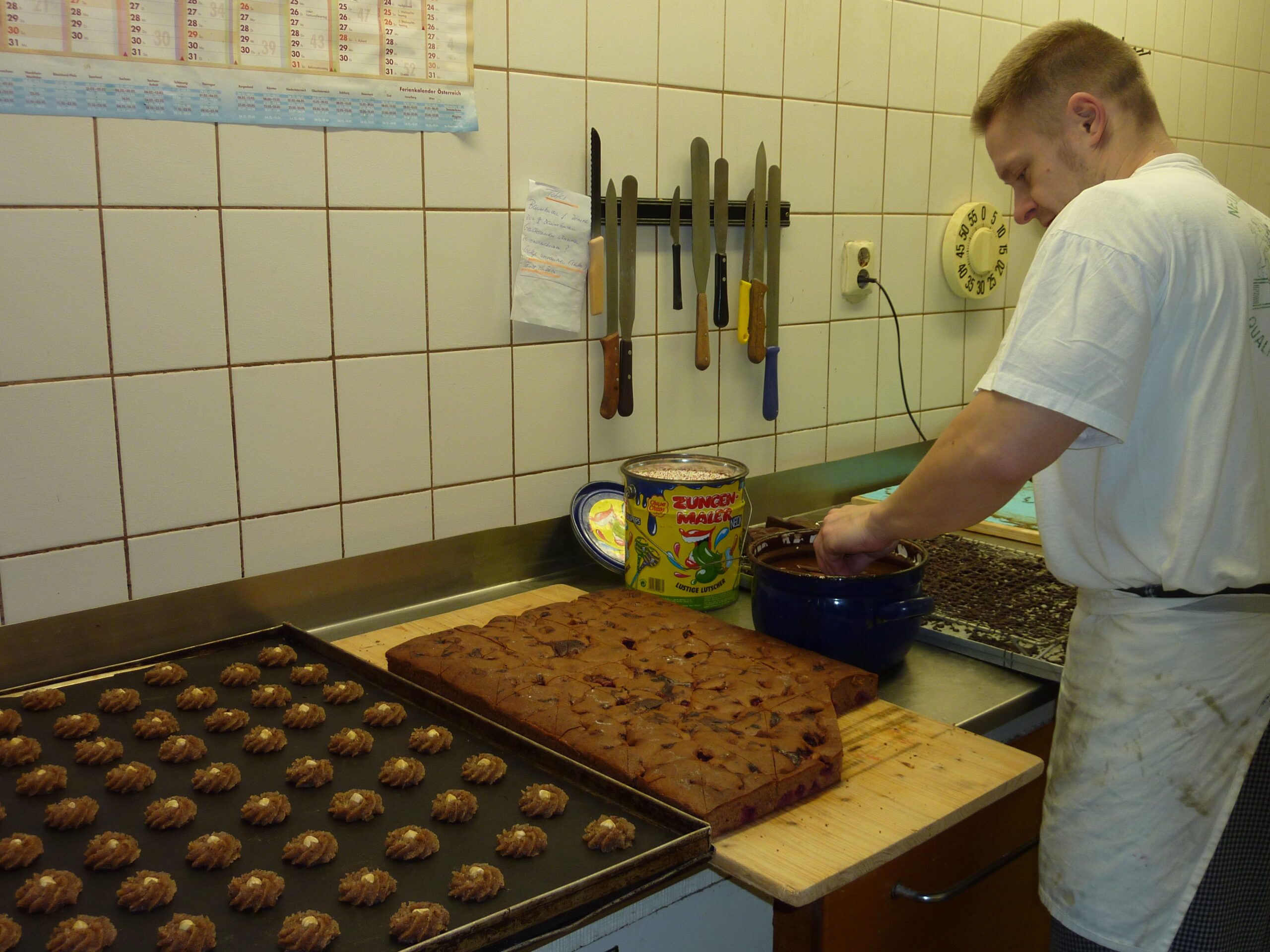 Bäcker taucht Gebäckstücke in Schokolade in der Backstube der Bäckerei Sachse