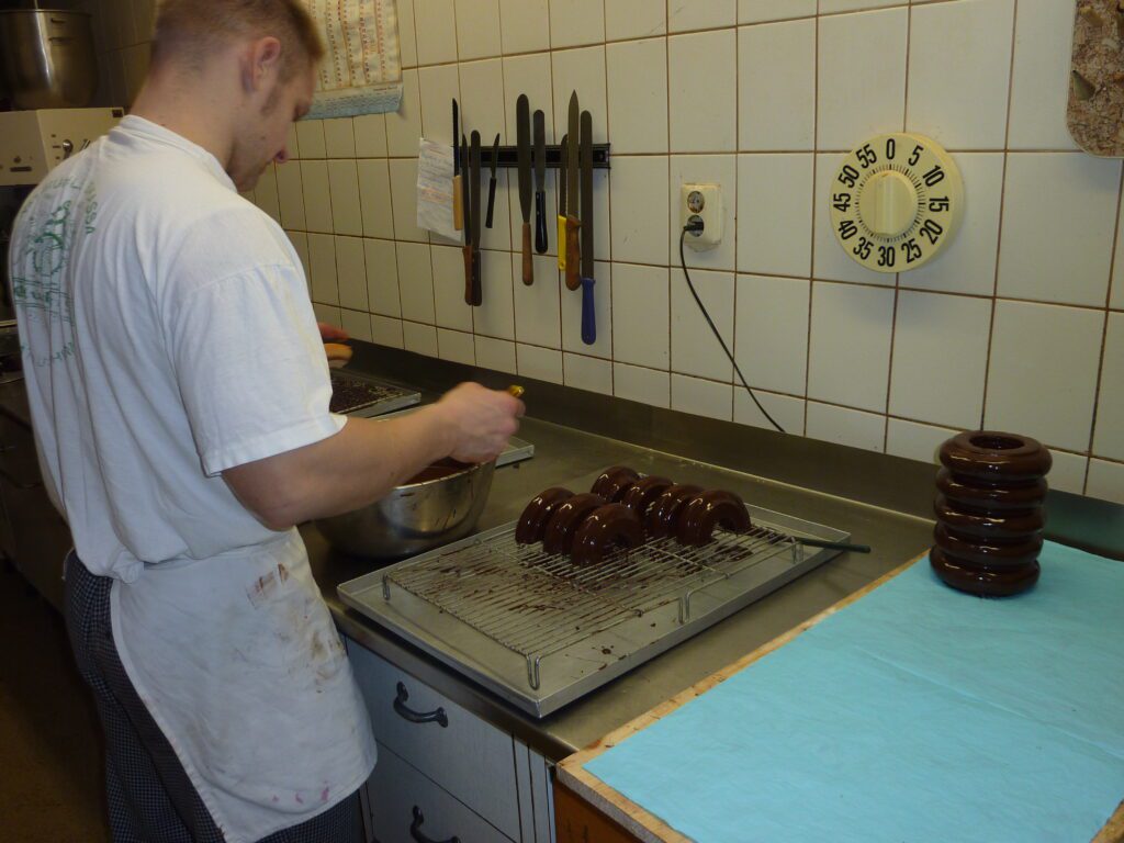 Bäcker glasiert Baumkuchenringe mit Schokolade in der Backstube der Bäckerei Sachse